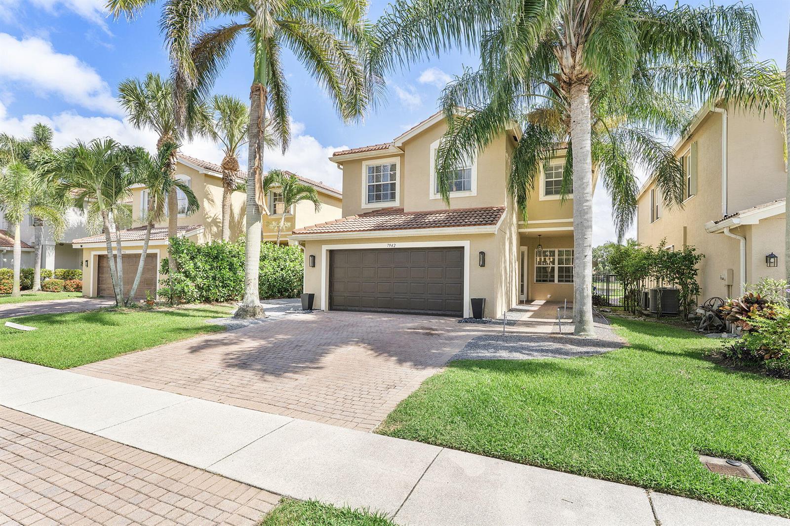 A two-story tan house with a brown garage door and palm trees in the front — 7942 Parsons Pine Drive, Boynton Beach FL 33437, BOYNTON BEACH, FL