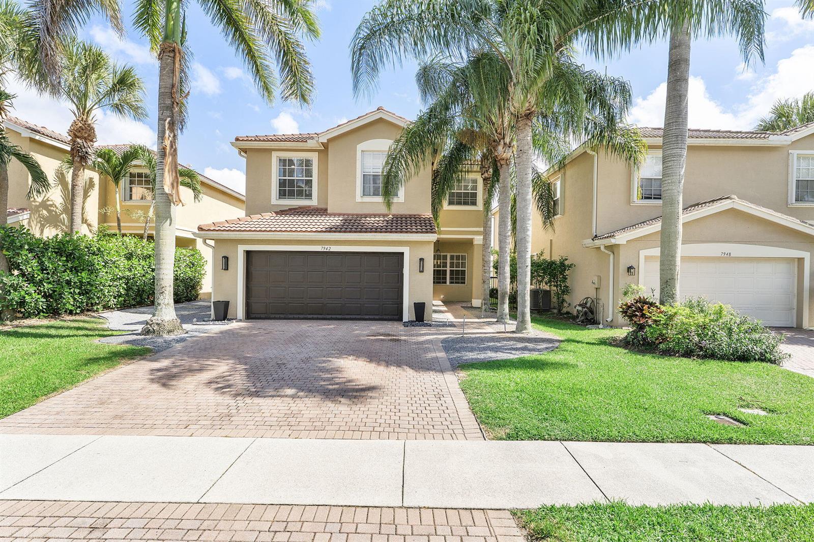 A two-story tan stucco house with a brown garage door and palm trees in front — 7942 Parsons Pine Drive, Boynton Beach FL 33437, BOYNTON BEACH, FL