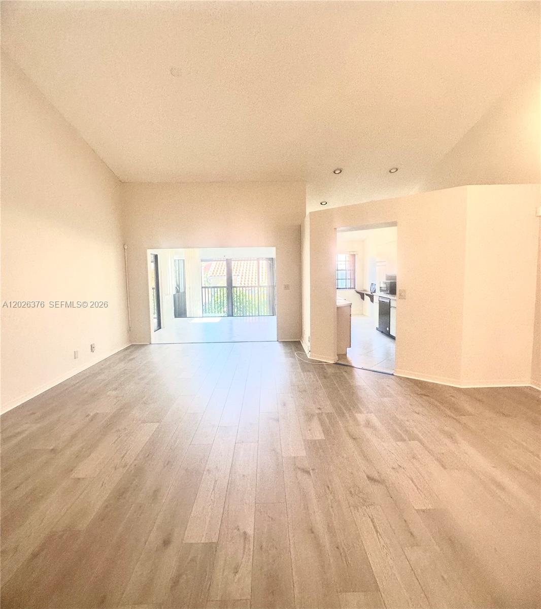 An open living area features light wood-look flooring, high ceilings, and a view of a balcony — 3176 Arbor Ln # 2506, Hollywood FL 33021, HOLLYWOOD, FL