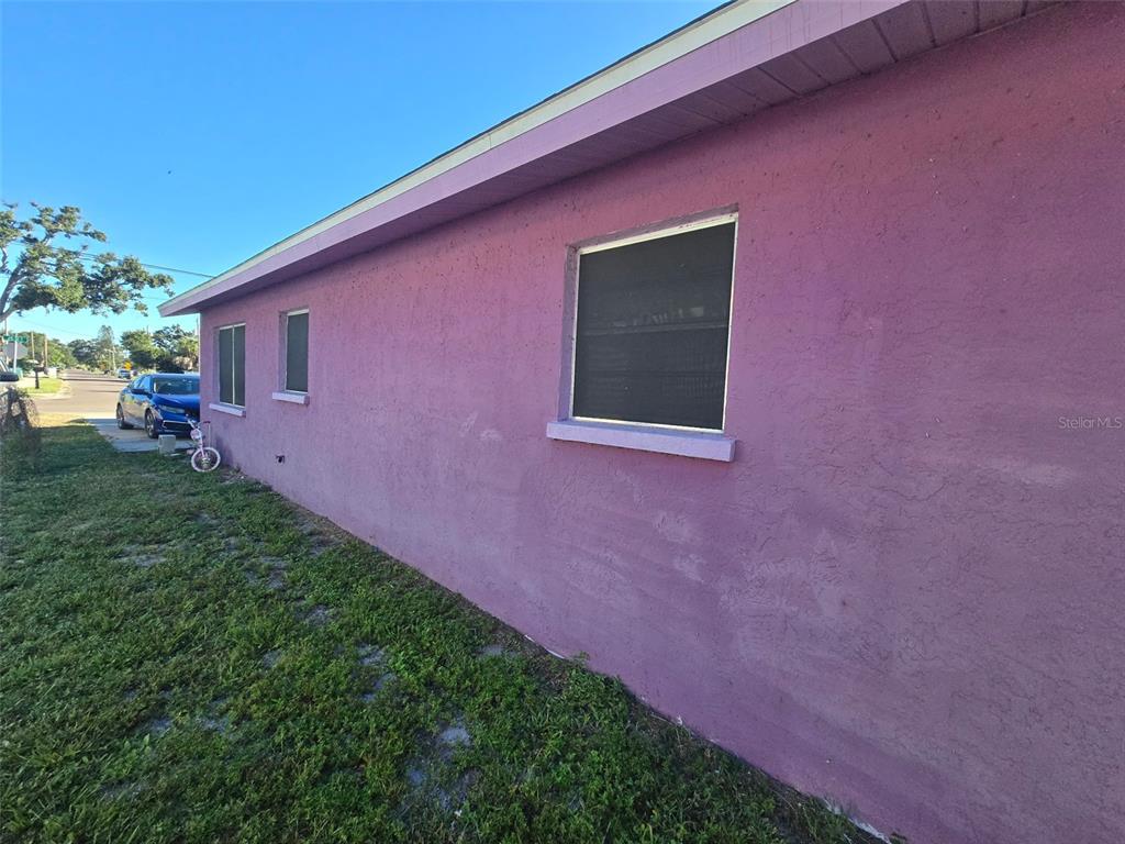 A side view of a purple stucco house exterior with three windows and a roof overhang — 503 25TH STREET E, PALMETTO, FL