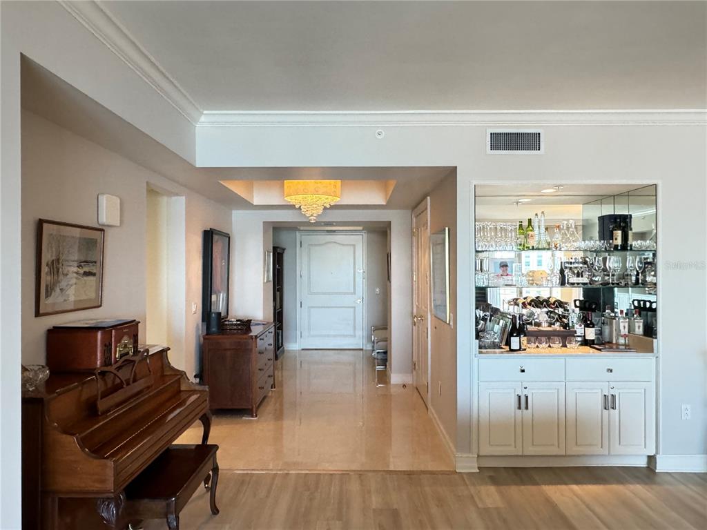 A foyer features a piano, a mirrored wet bar, and a chandelier leading to an entrance — 1111 RITZ CARLTON DRIVE UNIT 1404, SARASOTA, FL