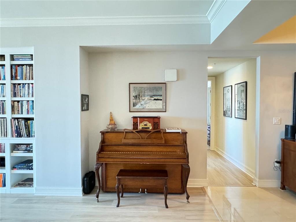 A wooden upright piano sits against a wall next to a built-in bookshelf — 1111 RITZ CARLTON DRIVE UNIT 1404, SARASOTA, FL