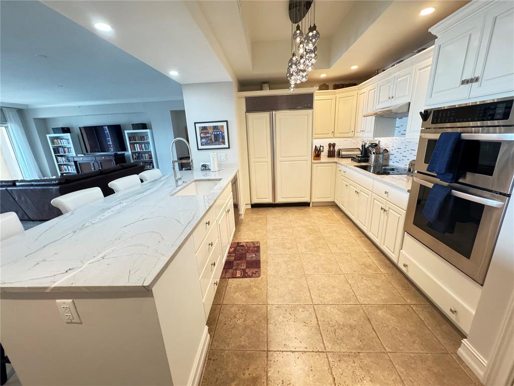 A kitchen features white cabinetry, a large marble-topped island, and stainless steel double ovens — 1111 RITZ CARLTON DRIVE UNIT 1404, SARASOTA, FL