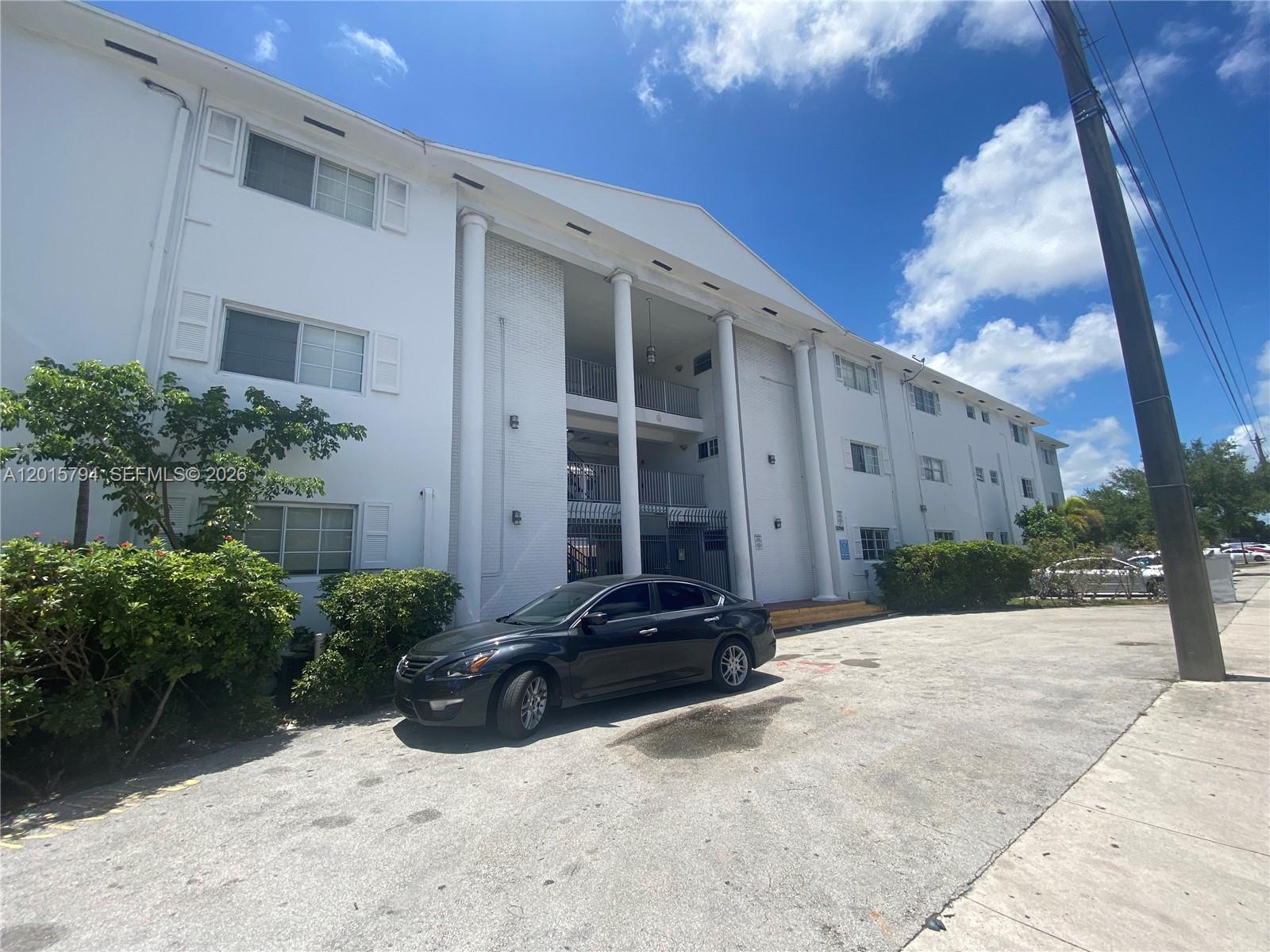A white multi-story apartment building features tall columns and a black car parked in front — 13700 NE 6th Ave # 115, North Miami FL 33161, NORTH MIAMI, FL