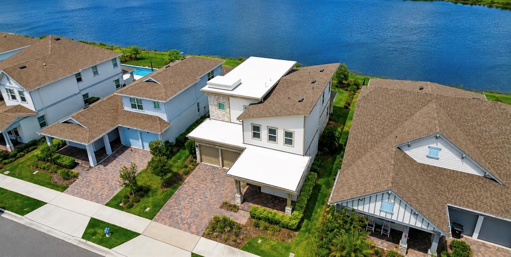 An aerial view shows three suburban houses with brown roofs situated along a waterfront — 13629 MCMILLAN DRIVE, ORLANDO, FL