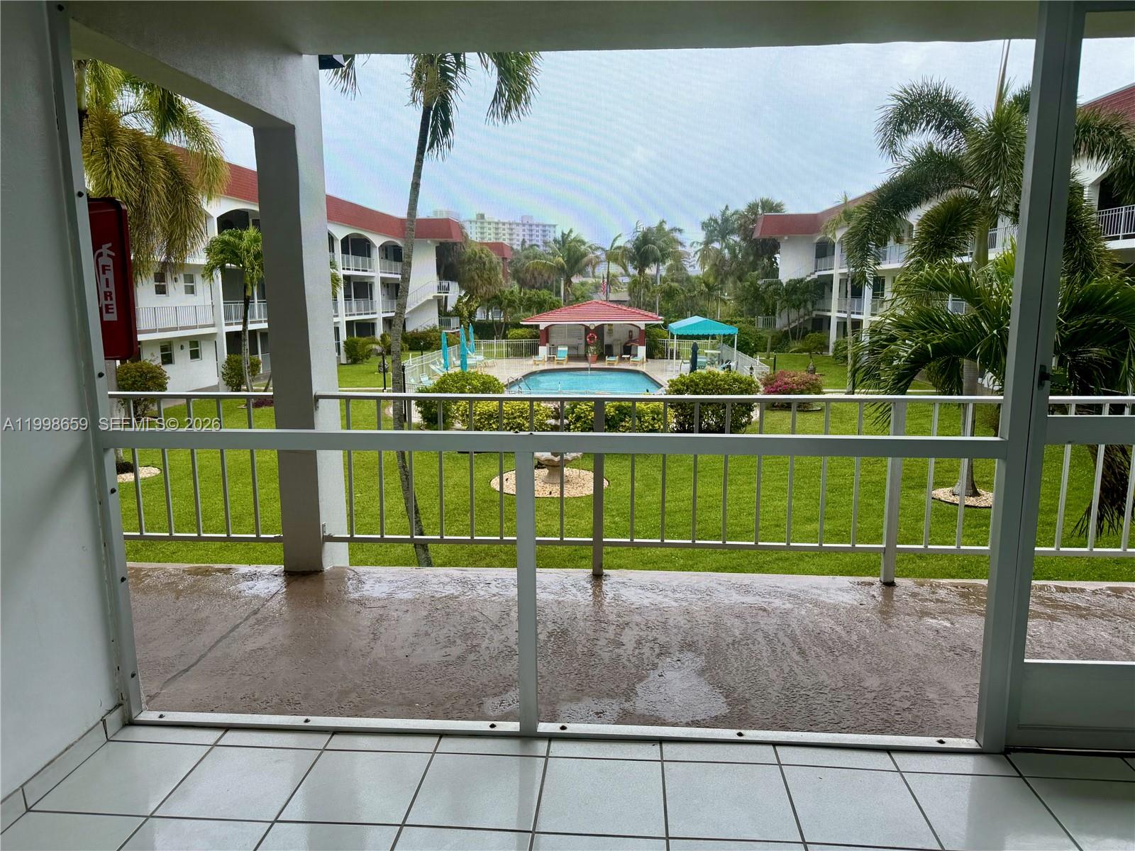 A screened balcony overlooks a courtyard with a swimming pool and surrounding apartment buildings — 580 Egret Dr # 212, Hallandale Beach FL 33009, HALLANDALE BEACH, FL