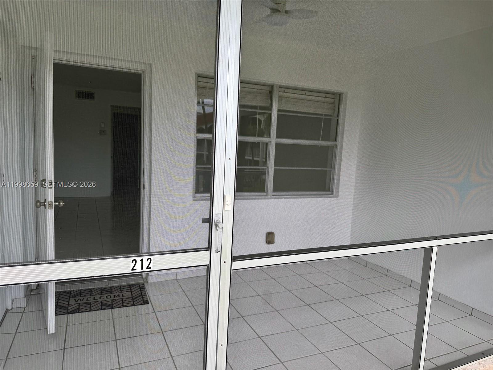 A screened-in porch features white tile flooring, a ceiling fan, and a numbered entry door — 580 Egret Dr # 212, Hallandale Beach FL 33009, HALLANDALE BEACH, FL
