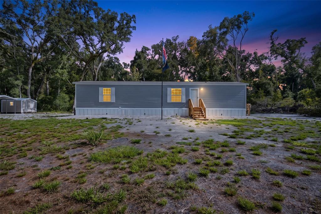 A single-story manufactured home with gray siding sits on a sandy lot at dusk — 311 NE 316TH AVENUE, OLD TOWN, FL