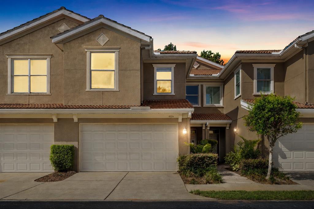 A two-story townhouse exterior features a beige stucco facade, a two-car garage, and tiled roofs — 4920 ANNISTON CIRCLE, TAMPA, FL