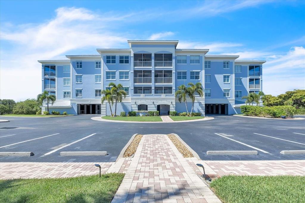 A multi-story blue apartment building stands behind a paved parking lot and walkway — 2001 BAL HARBOR BOULEVARD UNIT 2207, PUNTA GORDA, FL