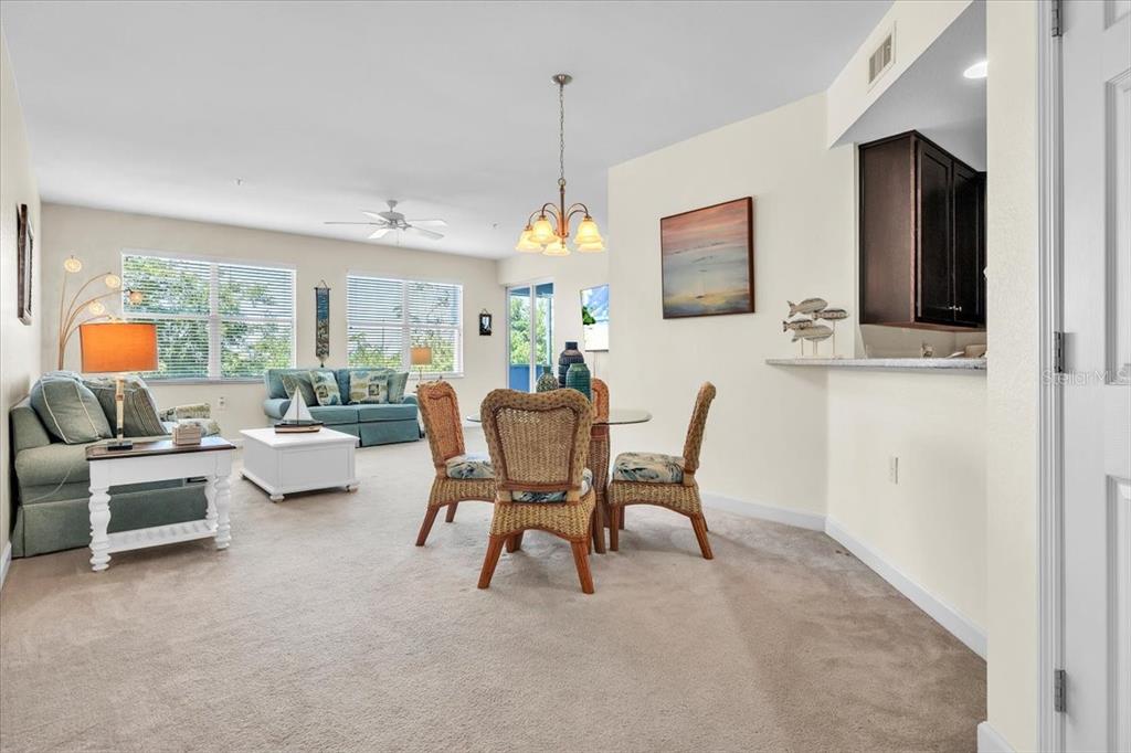 A living and dining area features beige carpet, wicker chairs, and a kitchen pass-through window — 2001 BAL HARBOR BOULEVARD UNIT 2207, PUNTA GORDA, FL