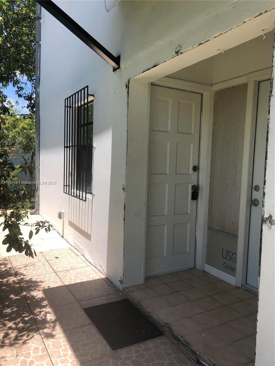 An exterior view shows a white building entrance with a tiled walkway and barred window — 1374 NE 176 st # 3, North Miami Beach FL 33162, NORTH MIAMI BEACH, FL