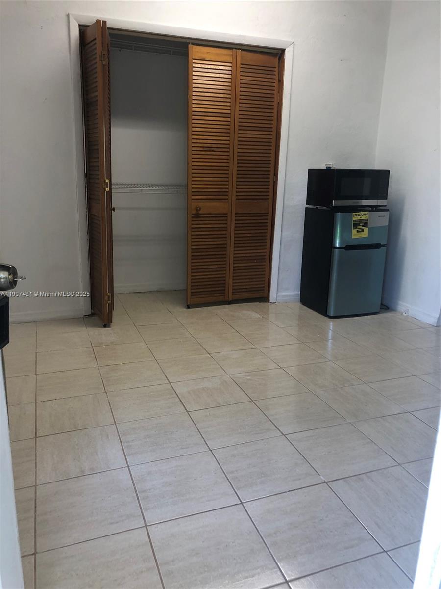 A room with tiled floors, a wooden louvered closet, and a small refrigerator with a microwave — 1374 NE 176 st # 3, North Miami Beach FL 33162, NORTH MIAMI BEACH, FL