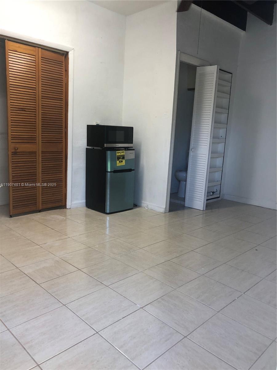 A room with light-colored tile flooring, a small refrigerator with a microwave, and two closets — 1374 NE 176 st # 3, North Miami Beach FL 33162, NORTH MIAMI BEACH, FL