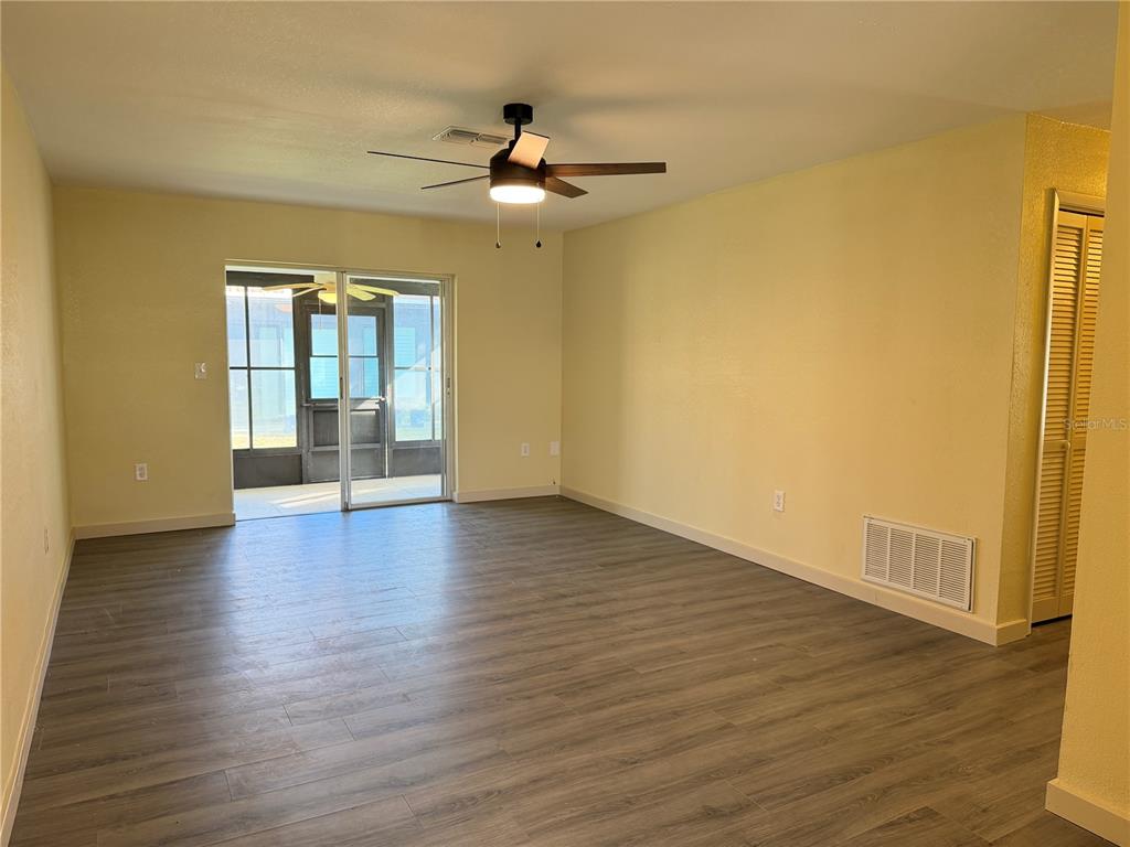 An empty living room with light yellow walls, wood-look flooring, and a sliding glass door — 9221 REPONDO PL, NEW PORT RICHEY, FL