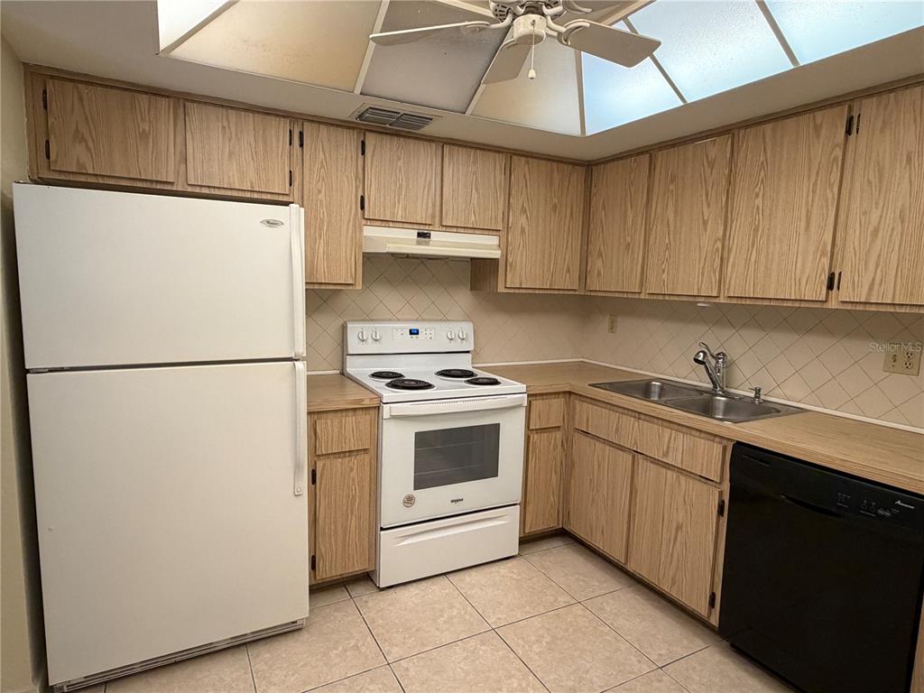 A kitchen features light wood cabinets, white appliances, a double sink, and tiled flooring — 9221 REPONDO PL, NEW PORT RICHEY, FL