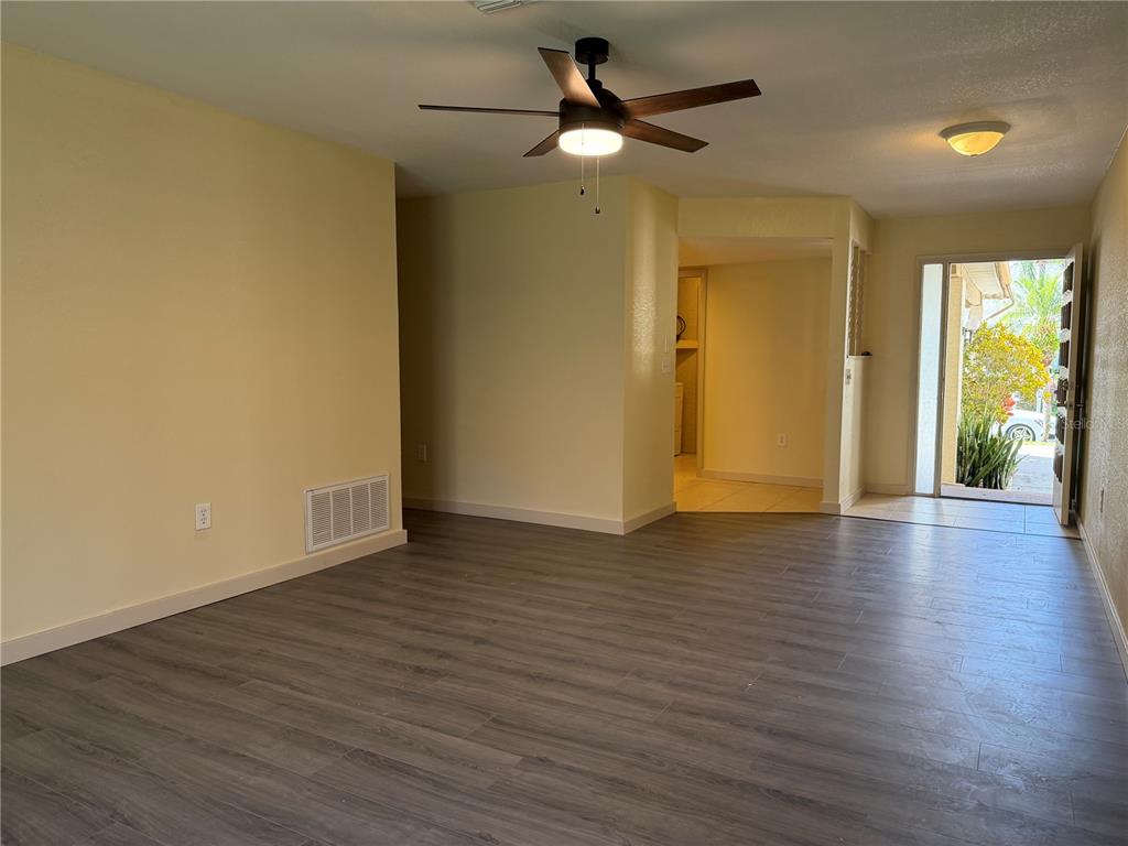 An interior view of a living room with wood-look flooring, a ceiling fan, and entryway — 9221 REPONDO PL, NEW PORT RICHEY, FL