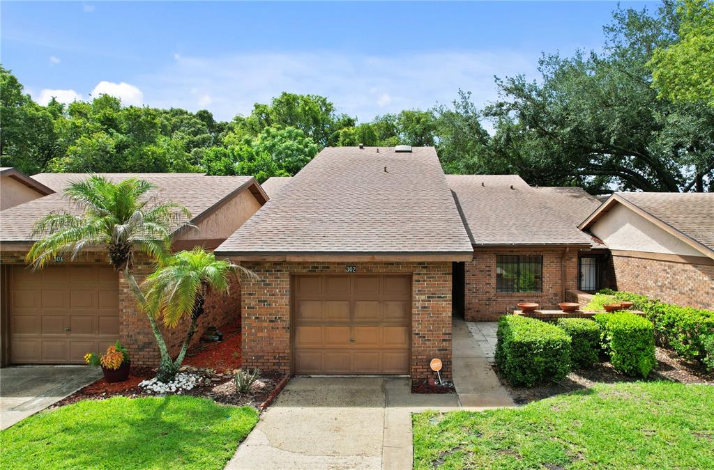 A brick townhouse exterior features a single-car garage, a palm tree, and manicured landscaping — 302 SAND TRAP COVE UNIT 302, LONGWOOD, FL