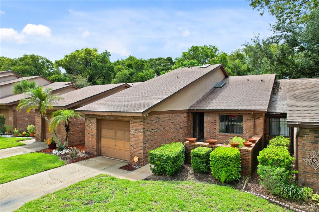A brick townhouse exterior features a single-car garage, a sloped roof, and landscaped front bushes — 302 SAND TRAP COVE UNIT 302, LONGWOOD, FL
