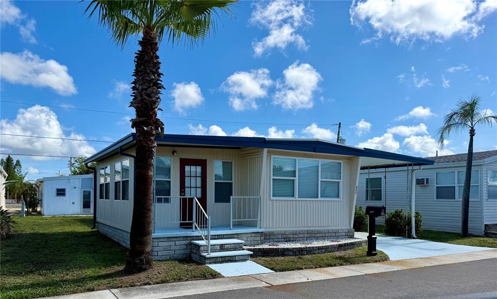 A single-story manufactured home with a palm tree, a small front porch, and a carport — 34527 VIOLET DRIVE N, PINELLAS PARK, FL