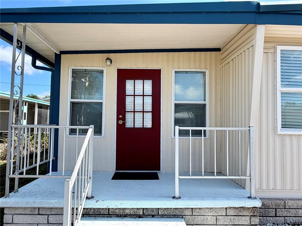 A red front door with a window sits on a porch with white metal railings — 34527 VIOLET DRIVE N, PINELLAS PARK, FL