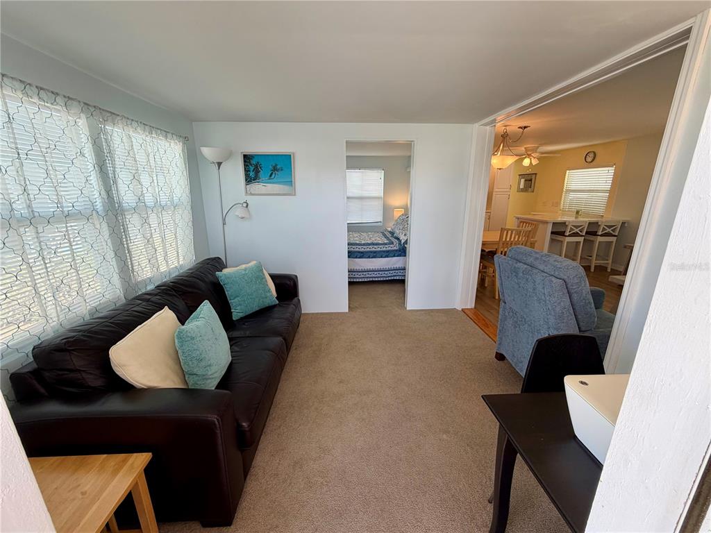 A living room with a dark leather sofa, carpeted floors, and a view into a kitchen — 34527 VIOLET DRIVE N, PINELLAS PARK, FL