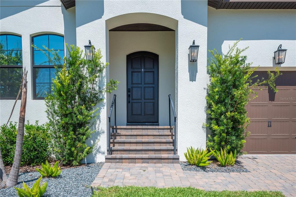 A front exterior view shows a dark arched door, brick steps, and two tall evergreen shrubs — 2403 DERBYSHIRE AVENUE, LAKELAND, FL