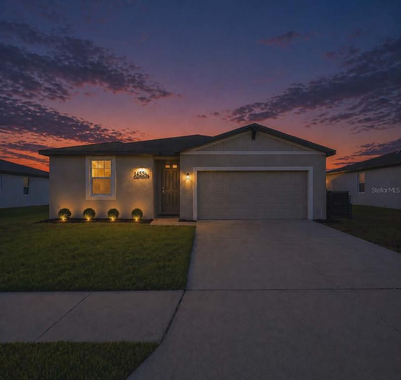 A single-story suburban house with a two-car garage and exterior landscape lighting at dusk — 1256 OAK VALLEY DRIVE, AUBURNDALE, FL