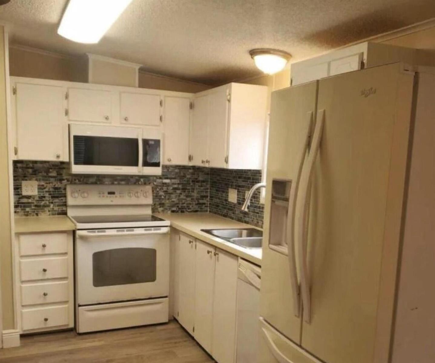 A kitchen with white cabinets, white appliances, a tiled backsplash, and light-colored countertops — 19418 Saddlebrook Court, FL 33903, FL