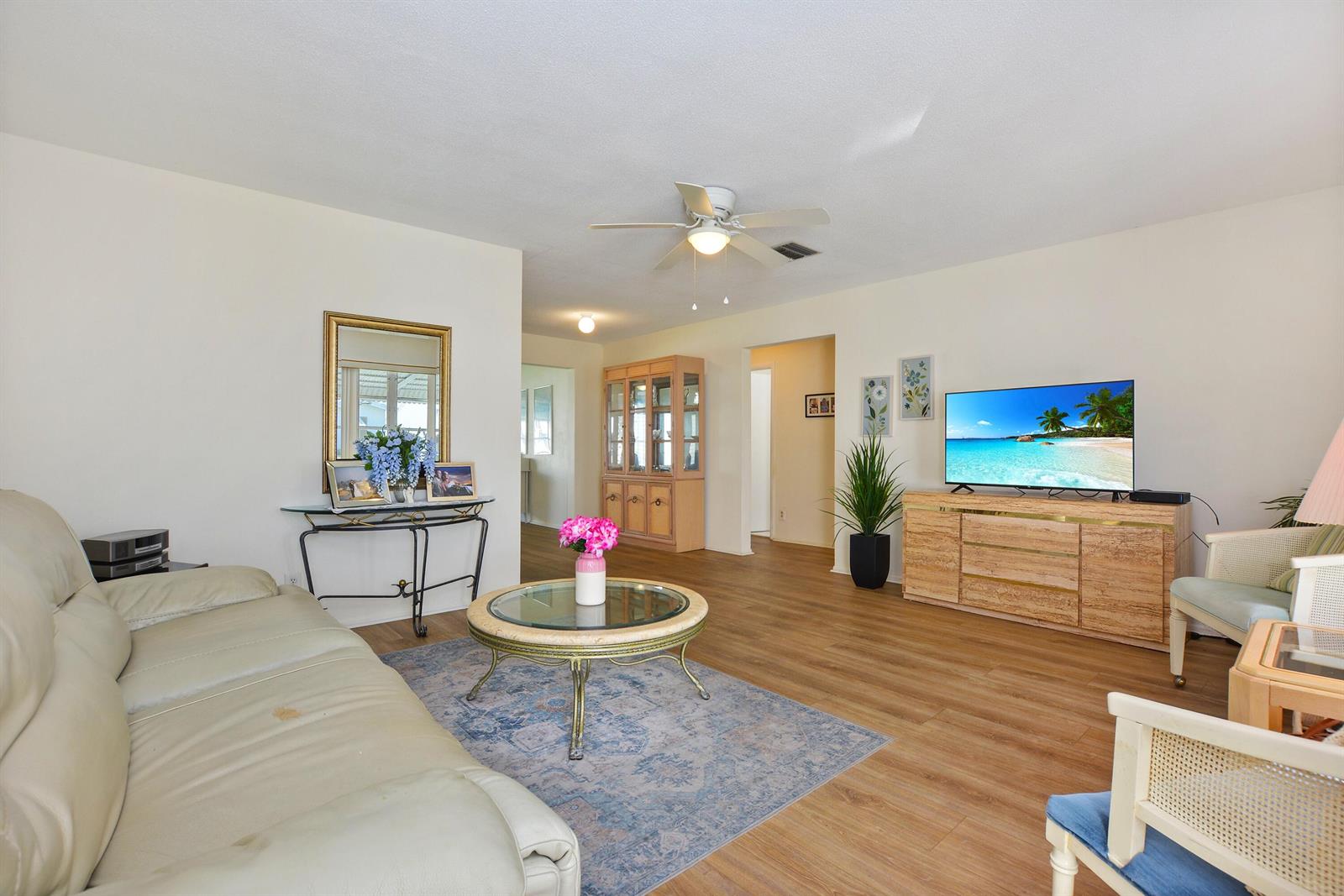 A living room features light wood flooring, a beige sofa, and a television on a console — 1005 Siesta Avenue, Boynton Beach FL 33426, BOYNTON BEACH, FL