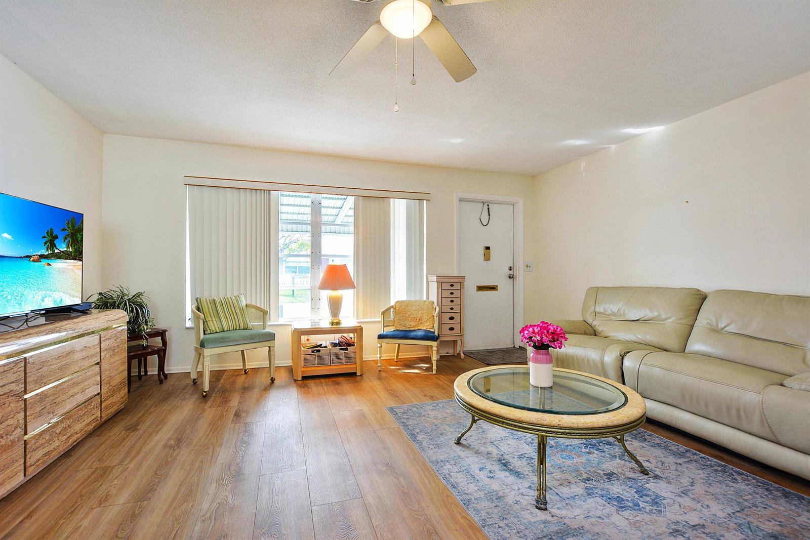 A living room features wood-look flooring, a beige leather sofa, a glass coffee table, and a television — 1005 Siesta Avenue, Boynton Beach FL 33426, BOYNTON BEACH, FL