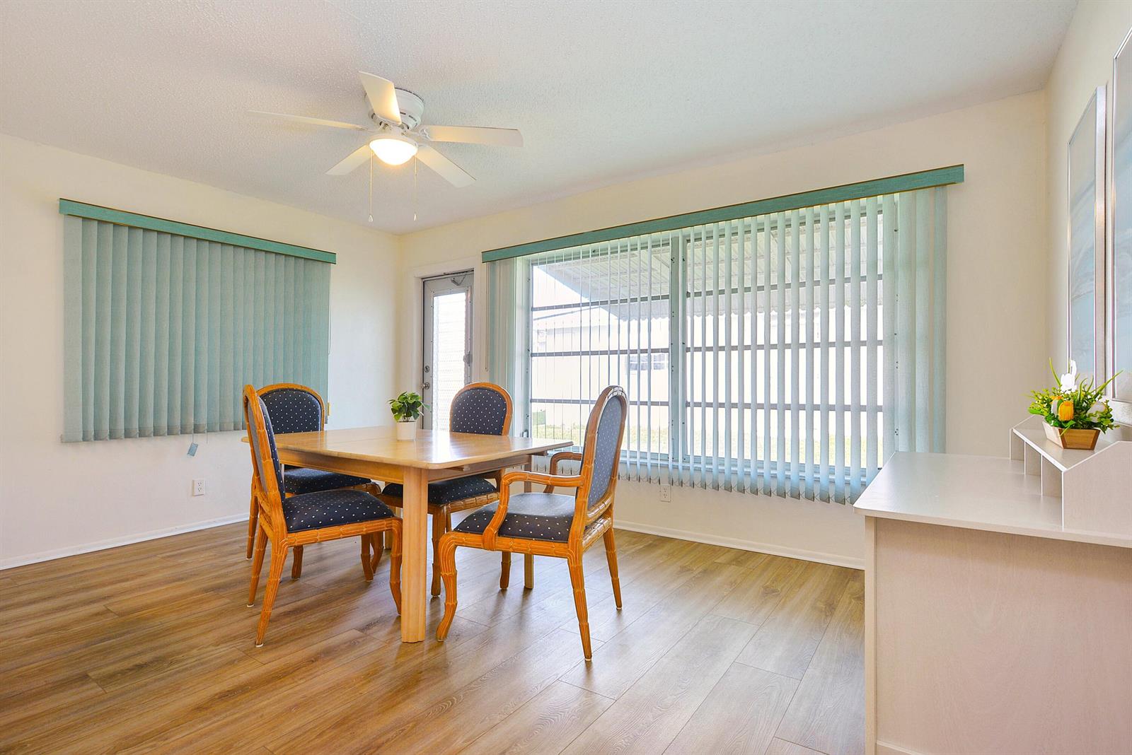 A dining room features a wooden table, four chairs, vertical blinds, and wood-look flooring — 1005 Siesta Avenue, Boynton Beach FL 33426, BOYNTON BEACH, FL