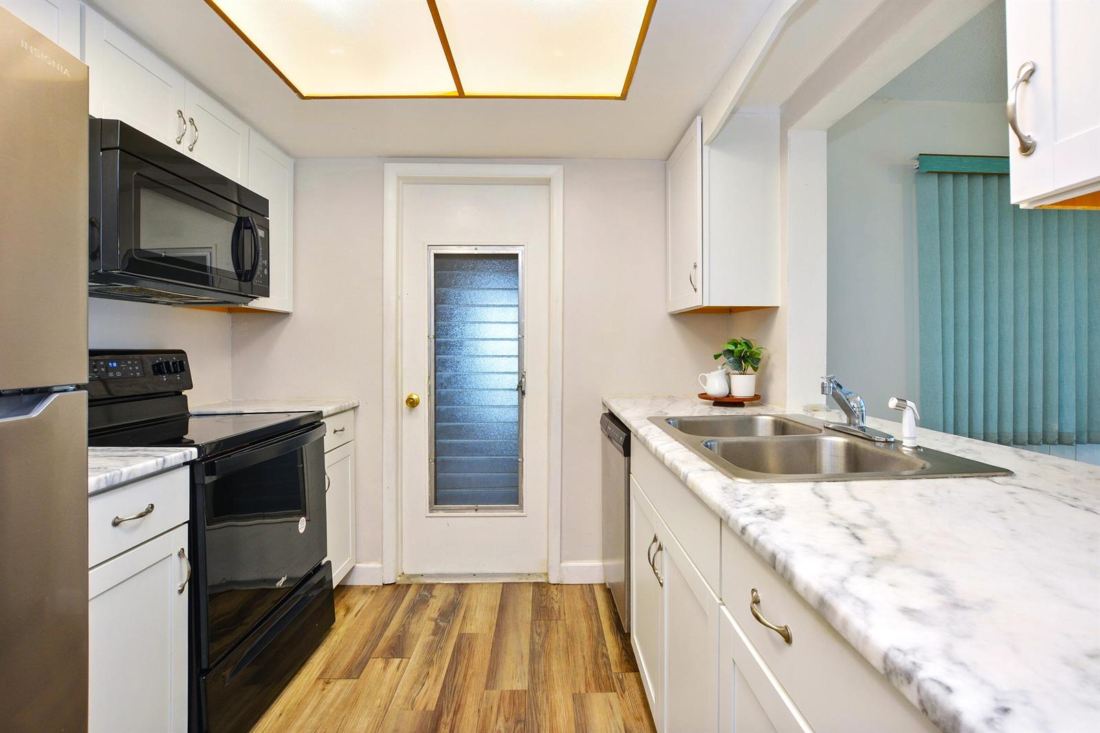 A kitchen features white cabinets, marble-look countertops, black appliances, and wood-look flooring — 1005 Siesta Avenue, Boynton Beach FL 33426, BOYNTON BEACH, FL
