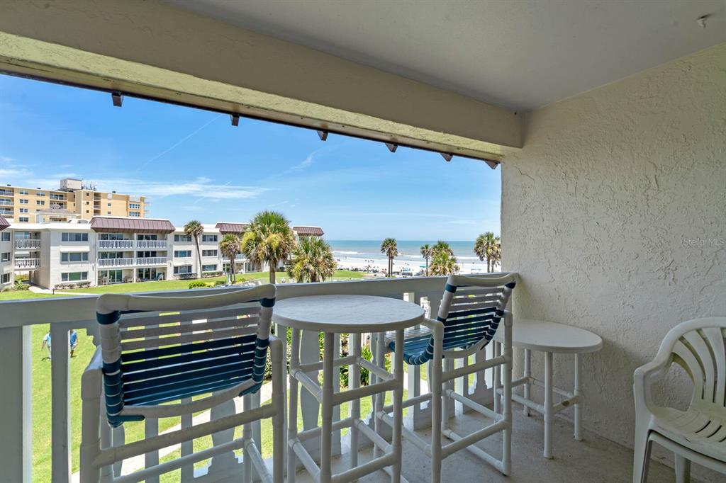 A balcony with patio furniture overlooks a grassy lawn, palm trees, and the ocean — 3663 S ATLANTIC AVENUE UNIT 31B, NEW SMYRNA BEACH, FL