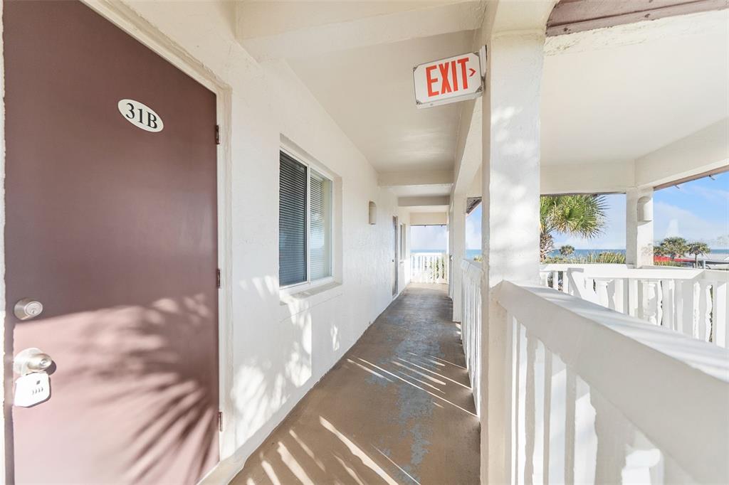 An outdoor hallway leads to a brown door labeled 31B with an ocean view beyond — 3663 S ATLANTIC AVENUE UNIT 31B, NEW SMYRNA BEACH, FL