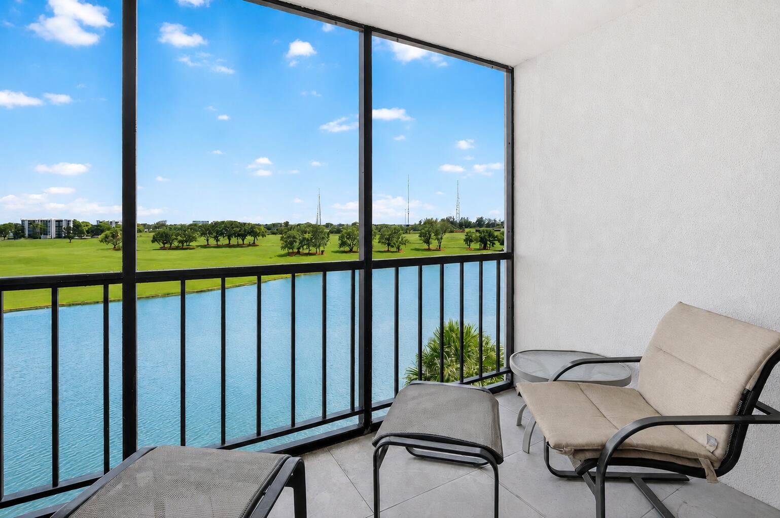 A screened-in balcony overlooks a lake and golf course with a chair and footstool — 7768 Lakeside Boulevard # 551, Boca Raton FL 33434, BOCA RATON, FL