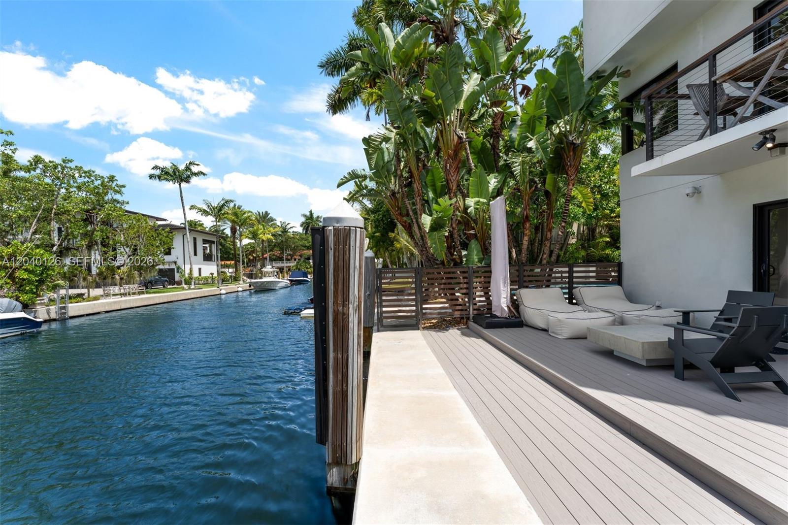 A wooden deck with lounge chairs overlooks a canal lined with palm trees and boats — 3560 W Fairview St, Miami FL 33133, MIAMI, FL