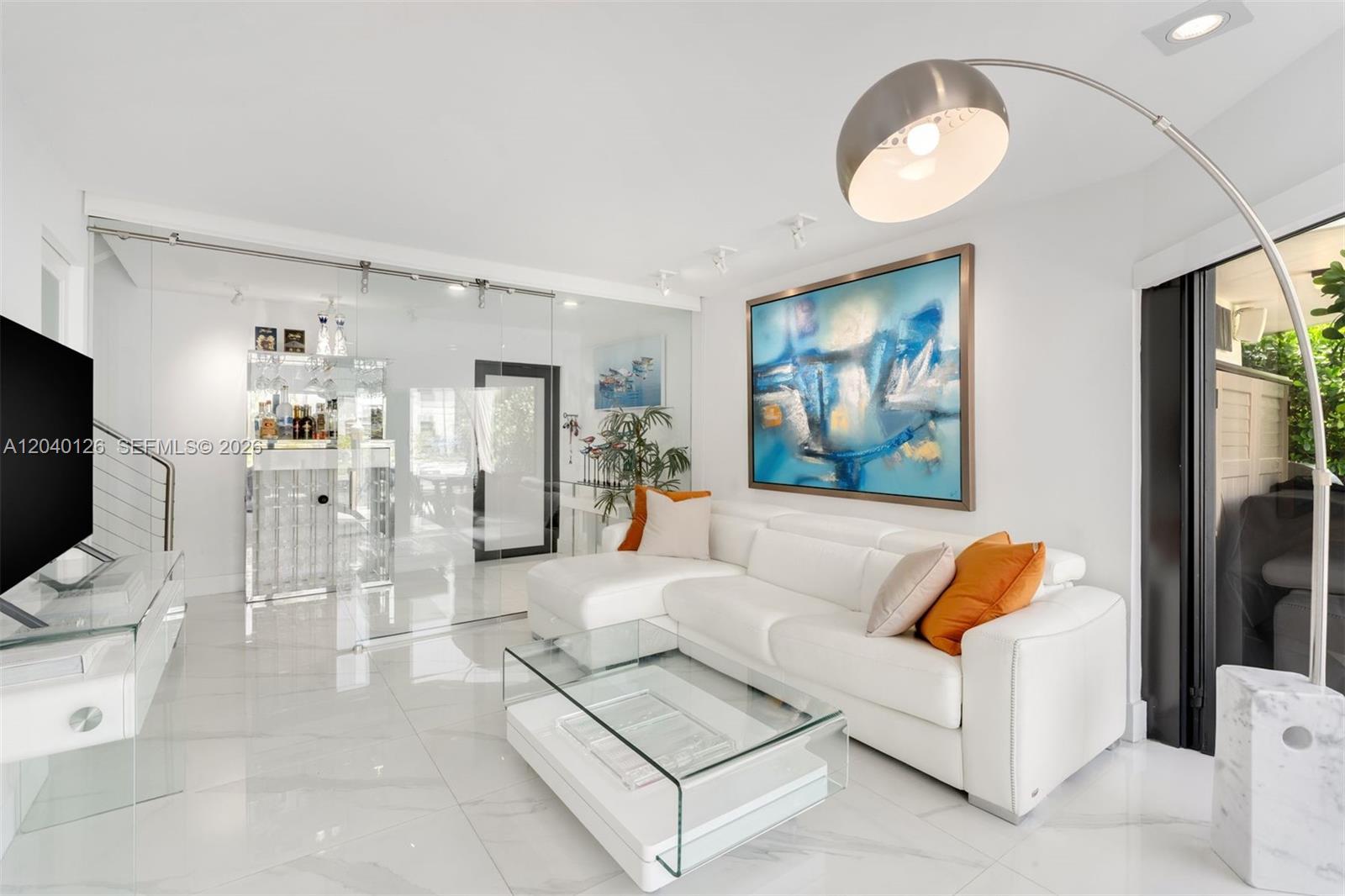 A modern living room features a white sectional sofa, glass coffee table, and glass-enclosed bar — 3560 W Fairview St, Miami FL 33133, MIAMI, FL