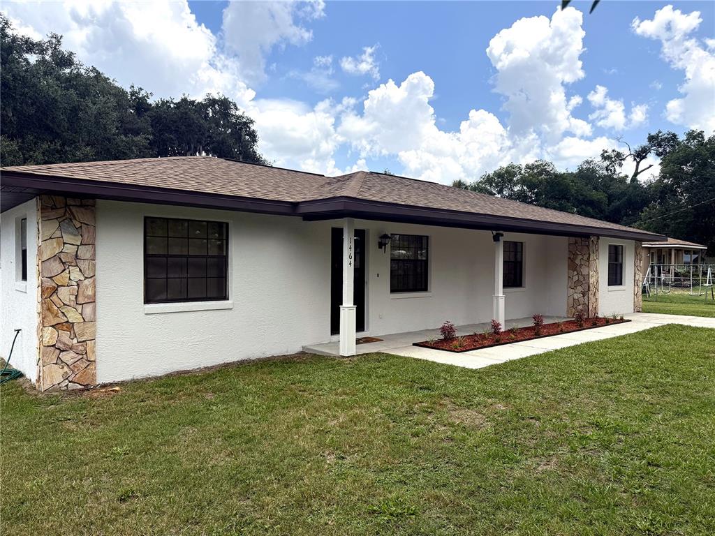 A single-story house with white stucco walls, stone accents, and a dark brown roof — 1464 SW 69TH ROAD, BUSHNELL, FL
