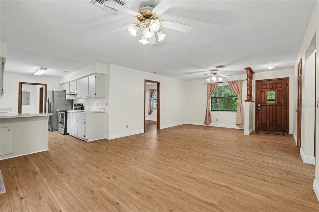 An open-concept living area with light wood-look flooring, white walls, and an adjacent kitchen — 1464 SW 69TH ROAD, BUSHNELL, FL