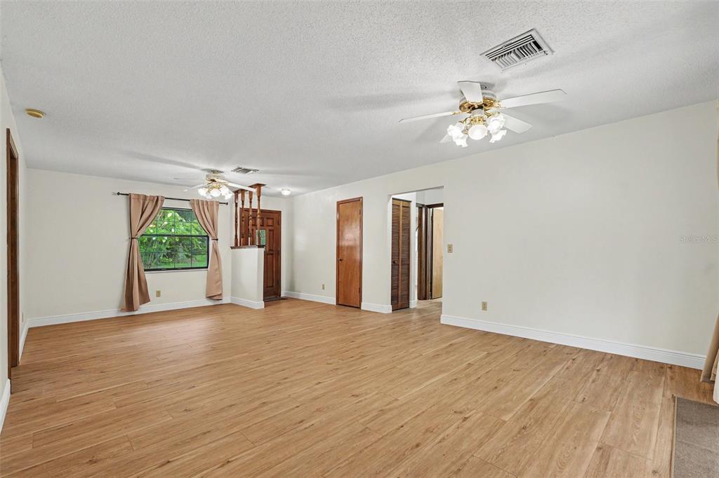 A spacious living room with light wood-look flooring, white walls, and two ceiling fans — 1464 SW 69TH ROAD, BUSHNELL, FL