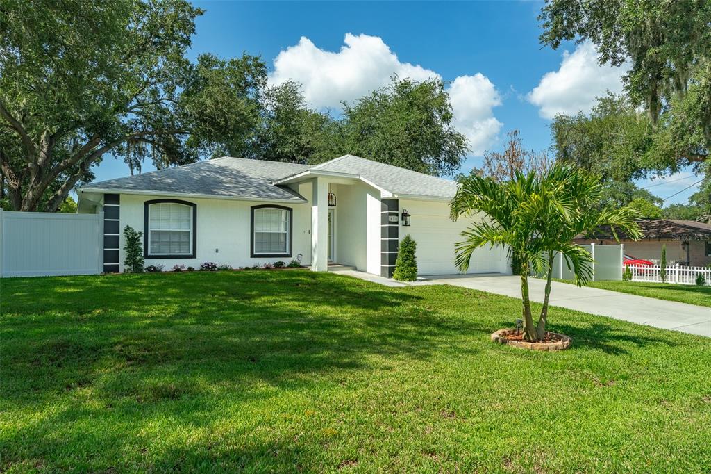 A white single-story house with a two-car garage, a green lawn, and a palm tree — 930 HICKS ROAD, LAKELAND, FL