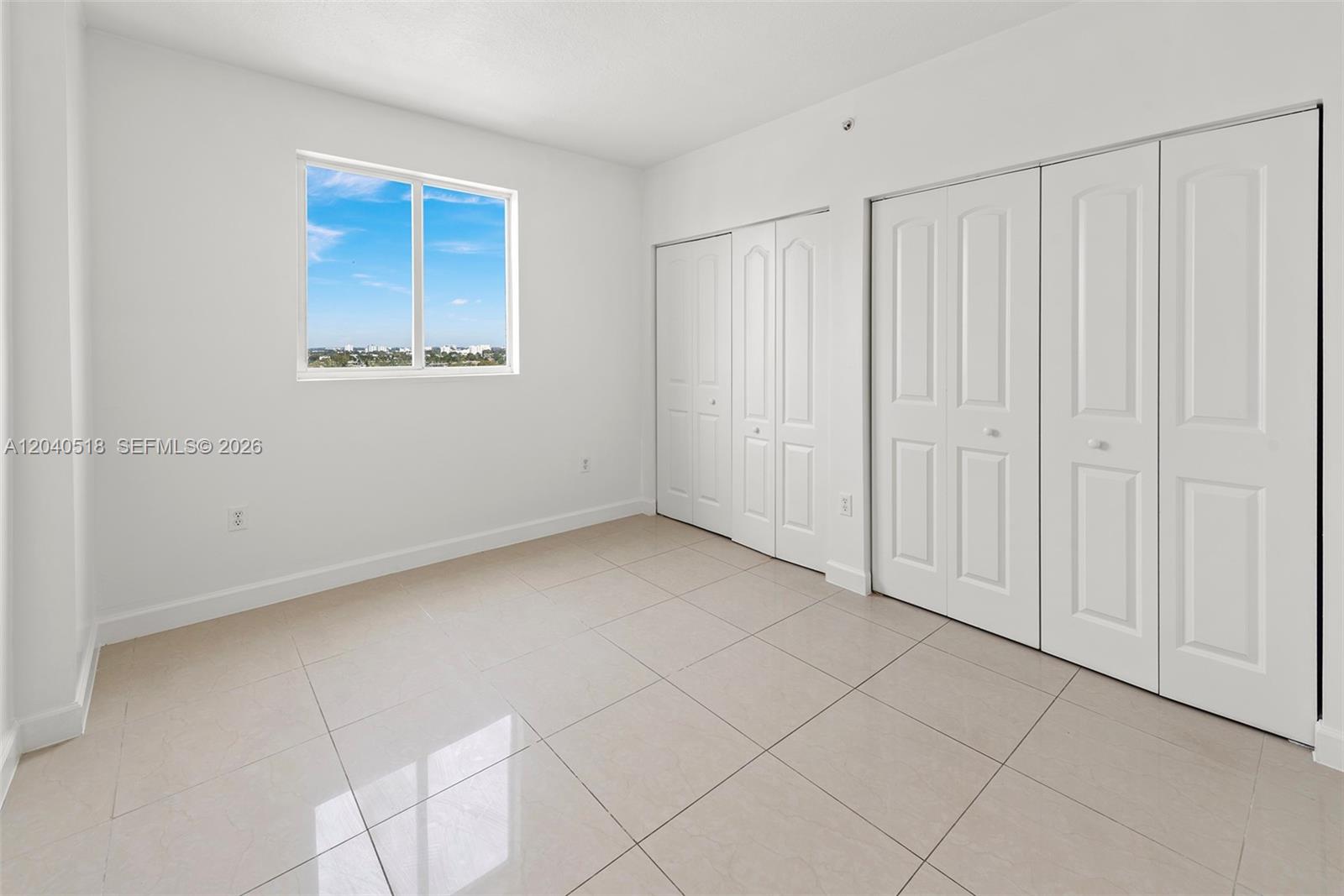 An empty bedroom features white walls, tile flooring, a window, and two sets of closets — 2217 NW 7th St # 1109, Miami FL 33125, MIAMI, FL