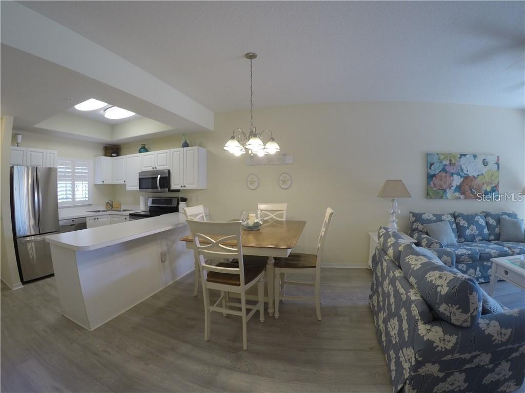 An open-concept kitchen and dining area with white cabinets, stainless appliances, and floral furniture — 4270 CASTLEBRIDGE LANE UNIT 1714B1, SARASOTA, FL
