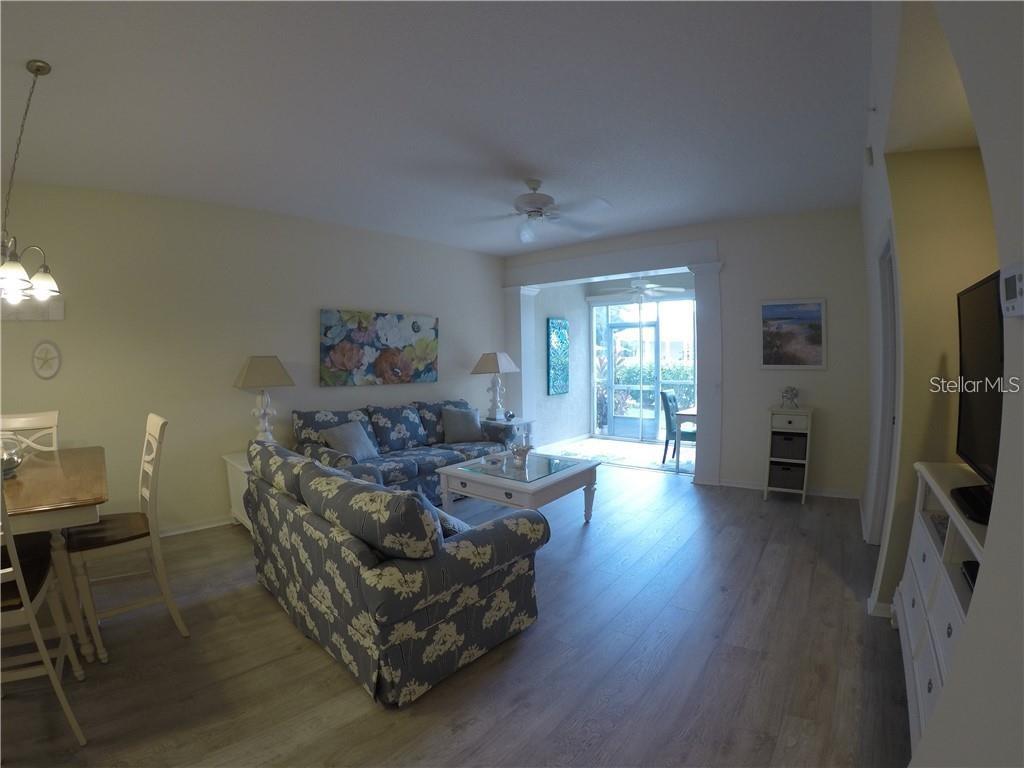 A living room and dining area with floral sofas, light wood flooring, and a sliding door — 4270 CASTLEBRIDGE LANE UNIT 1714B1, SARASOTA, FL