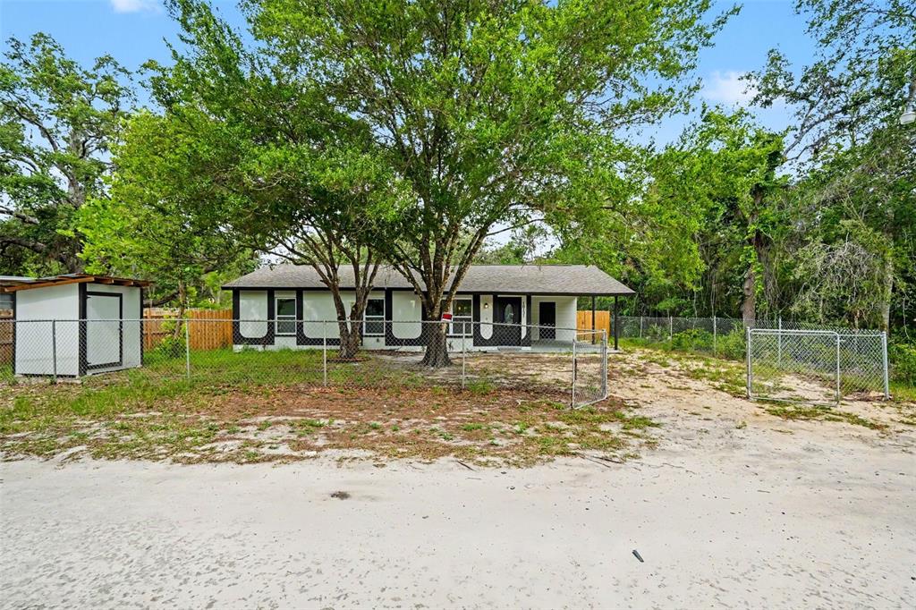 A single-story house with a fenced yard and large trees sits on a sandy lot — 10131 FIELD STREET, NEW PORT RICHEY, FL
