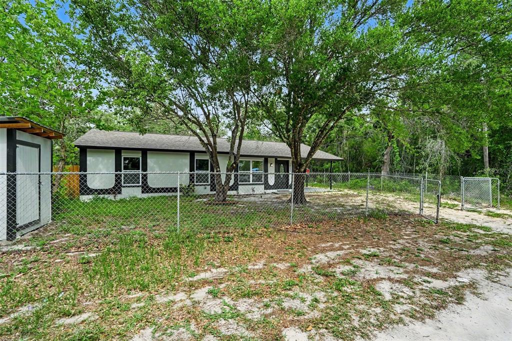 A single-story house with a white exterior and dark trim sits behind a chain-link fence — 10131 FIELD STREET, NEW PORT RICHEY, FL