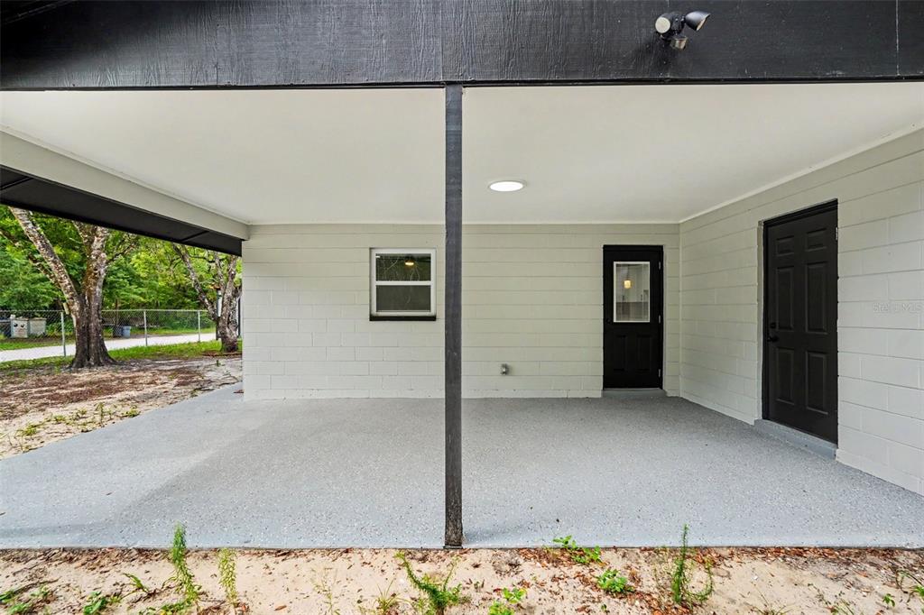A covered concrete patio features a light gray block wall, two black doors, and windows — 10131 FIELD STREET, NEW PORT RICHEY, FL