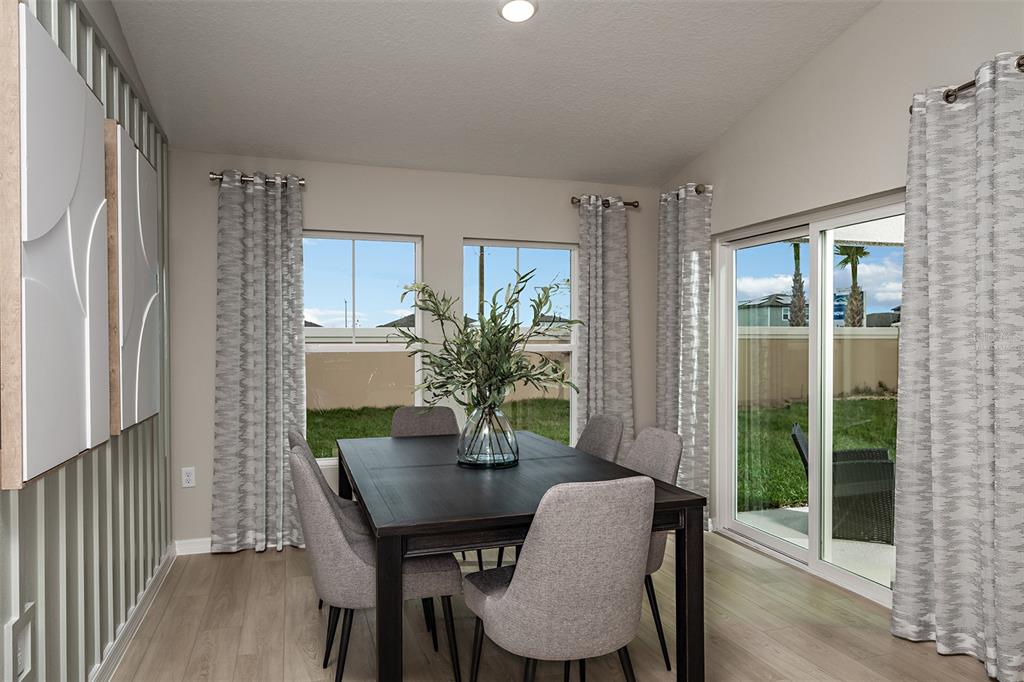 A dining room features a dark wood table, gray upholstered chairs, and sliding glass doors — 9273 ORCHARD PARK LANE, ZEPHYRHILLS, FL