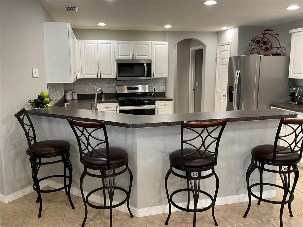 A kitchen features white cabinetry, stainless steel appliances, a dark countertop, and four bar stools — 532 DOLCETTO DRIVE, DAVENPORT, FL